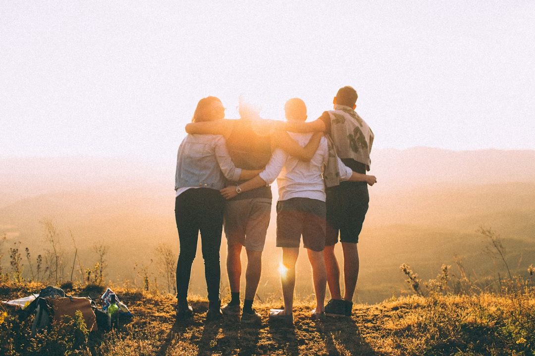 A group of friends standing together outdoors at sunset, arms around each other