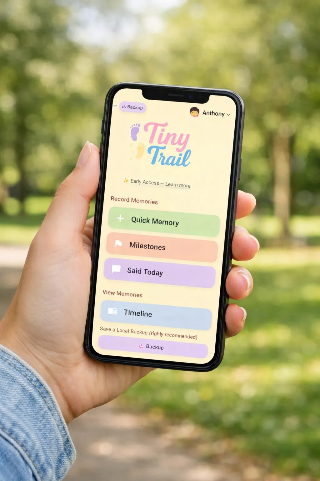A hand holding a phone showing the Tiny Trail app open in a park